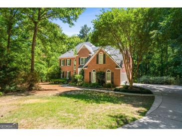 Brick house with a two-car garage and large front yard, surrounded by lush greenery at 2215 Whispering Pines Ln, Mcdonough, GA 30253