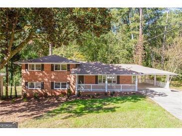 Charming red brick home with mature trees, front porch, and covered carport on a sunny day at 504 Milligan Dr, Stone Mountain, GA 30083