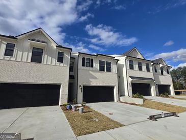Newly built townhomes with brick facades, black garages, concrete driveways, and bright blue skies at 1935 Westwind Street # 157, Lawrenceville, GA 30043
