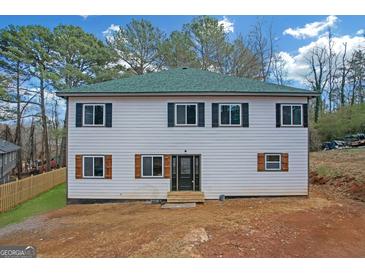 Two-story home with light siding, dark shutters, and a green roof, set in a wooded area at 6274 Booker Ln, Lithonia, GA 30058