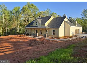 New construction home featuring light yellow siding, a dark gray roof, and an attached garage in a wooded area at Lot C Montannas Way, Moreland, GA 30259