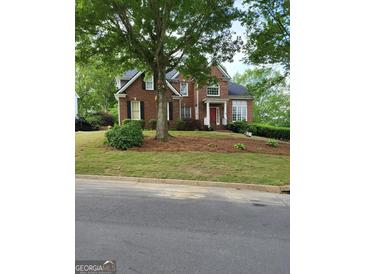 Charming two-story brick home with a red front door and well-manicured lawn, surrounded by mature trees in a lush neighborhood at 6410 E Hills Ct, Cumming, GA 30041