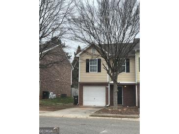 Two-story townhome with neutral siding, black shutters, a one-car garage, and a brick accent wall at 305 Magnolia Gardens Walk, Mcdonough, GA 30253