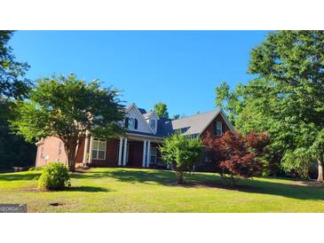 Traditional brick home featuring a manicured lawn, mature landscaping, and a welcoming front porch at 35 Abelia Dr, Covington, GA 30014