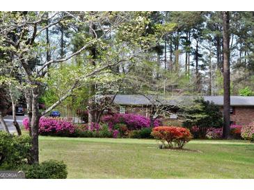 Beautifully landscaped front yard with mature trees, flowering shrubs, and a glimpse of a charming brick home at 160 Pine Trail Rd, Fayetteville, GA 30214