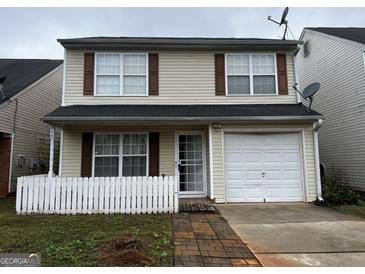 Charming two-story home with tan siding, brown shutters, a white picket fence, and an attached one-car garage at 419 Kara Ln, Mcdonough, GA 30253