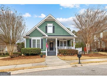 Charming green home featuring a welcoming front porch, manicured landscaping, and an American flag at 155 Stayman Park, Fayetteville, GA 30215