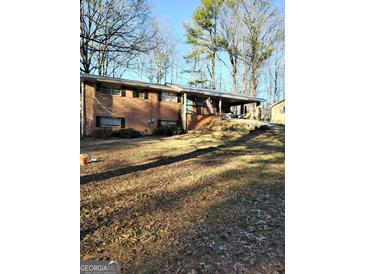 A charming, one-story brick home featuring a large, covered porch, set against a backdrop of mature trees at 4651 Palm Dr, Douglasville, GA 30135