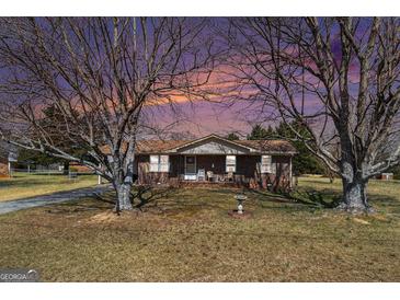 Charming brick ranch home featuring a well-manicured lawn, mature trees, and a cozy front porch with rocking chairs at 143 Teamon Rd, Hampton, GA 30228