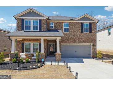 Two-story home featuring stone accents, a two-car garage, manicured landscaping, and a welcoming covered front porch at 6910 Newcastle Ct, Fairburn, GA 30213
