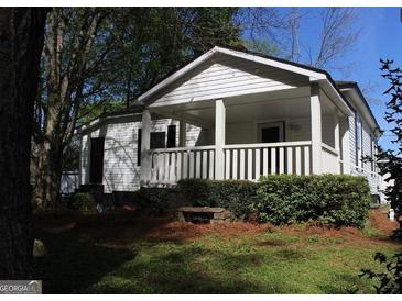 Charming single story home featuring a covered front porch, lush landscaping, and mature trees at 1 Maple St, Porterdale, GA 30014