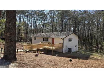 Charming home exterior featuring a wooden deck and a red front door, surrounded by a lush, wooded landscape at 3189 Fern Ridge Ne Dr, Conyers, GA 30013