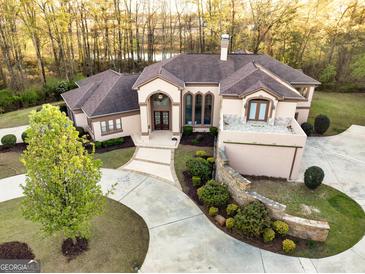 Aerial view of a luxurious, light pink stucco home with a winding driveway and professionally landscaped front yard near a lake at 2279 Fieldstone Dr, Conyers, GA 30013
