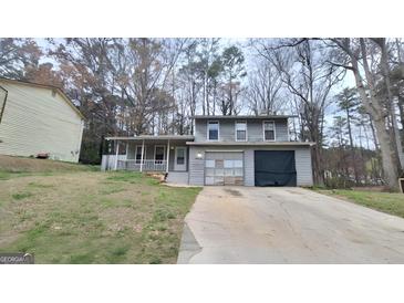 Two-story home featuring a covered porch, attached garage, and a concrete driveway surrounded by mature trees at 4812 White Oak Path, Stone Mountain, GA 30088