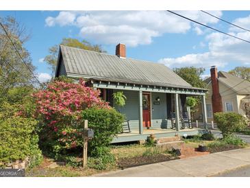 Charming home featuring a metal roof, inviting front porch, and vibrant landscaping with colorful azaleas at 1009 Institute Nw St, Conyers, GA 30012