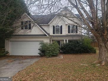 Two-story home featuring white siding, a two-car garage, and a front yard landscaped with bushes and mature trees at 50 Village Walk, Covington, GA 30016