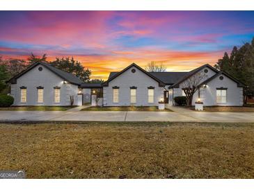 Stunning white brick home with black roof, green lawn, and picturesque sunset sky at 2615 Hampton Locust Grove Rd, Locust Grove, GA 30248