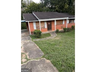 Exterior shot of a boarded up red brick home with an overgrown lawn and sidewalk at 1827 Thomasville Se Dr, Atlanta, GA 30315