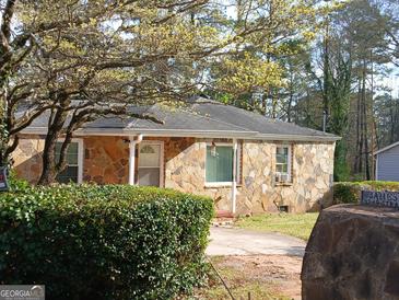 Charming stone house with a well-manicured lawn and a tree with yellow flowers in front at 3249 E Stratton Ln, Scottdale, GA 30079