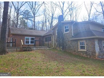 View of the home's exterior featuring a stone chimney, brick siding, and a deck with lattice at 3314 Henson Ln, Stockbridge, GA 30281