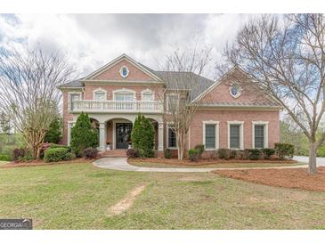 Grand two-story brick home with a covered balcony, columned entryway, and professionally landscaped front yard at 217 Brunswick Dr, Tyrone, GA 30290