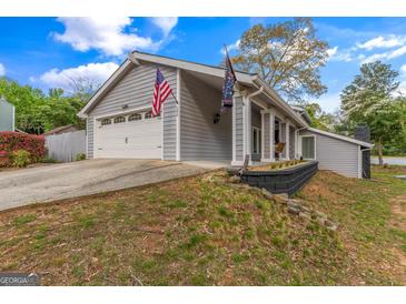 Charming home featuring a two-car garage and American flags, set against a backdrop of mature trees and sky at 205 Raintree Bnd, Peachtree City, GA 30269