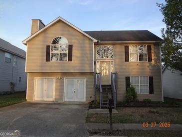 Two-story tan home with a chimney, dark shutters, a basement garage, and a small set of stairs at 2338 Rambling Way, Lithonia, GA 30058
