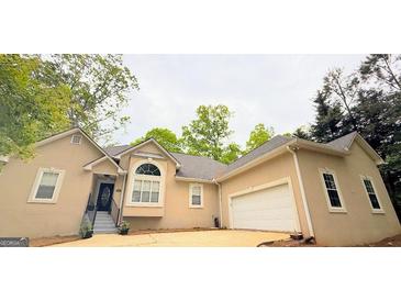Beige home featuring an attached garage, front yard, and well-manicured landscaping at 1252 Heritage Dr, Villa Rica, GA 30180