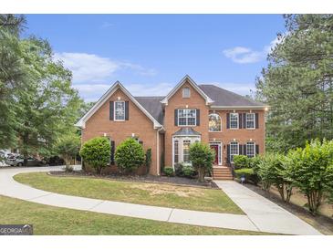 Traditional brick home featuring a manicured lawn, mature trees, and a charming red front door at 1085 Crown River Pkwy, Mcdonough, GA 30252