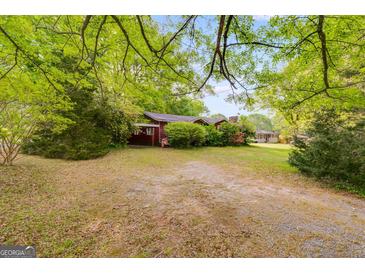 View of the front yard and exterior of the red home surrounded by mature trees and landscaping at 362 Highway 113, Temple, GA 30179