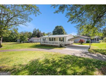 Charming one-story home with covered porch, carport and well-maintained lawn on a sunny day at 73 Highpoint Ln, Locust Grove, GA 30248