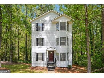 Charming three-story home with white siding, black shutters and trim surrounded by lush, mature trees at 4448 Janice Dr, Snellville, GA 30039