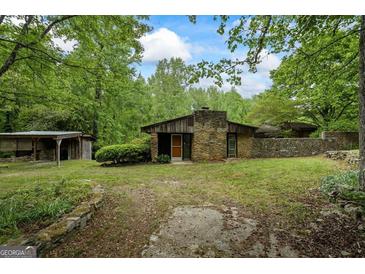 Charming single-story home with a stone facade, wood accents, and a covered storage building surrounded by lush greenery at 5493 Alexanders Lake Sw Rd, Stockbridge, GA 30281