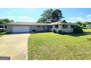 Charming one-story home with an attached garage, green lawn, and an American flag at 140 Whitehead Sw Rd, Oxford, GA 30054
