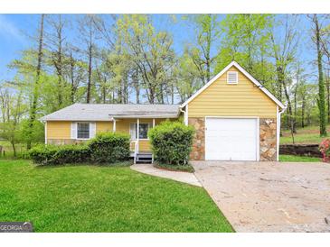 Charming home with a yellow exterior, stone accents, attached garage and green lawn at 5998 Radford Dr, Riverdale, GA 30296