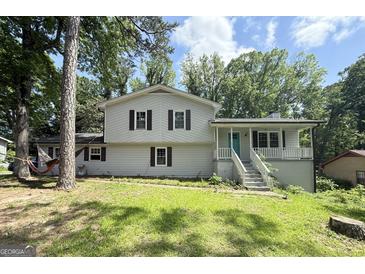 Charming two-story home with a front yard and a blue door on the porch, surrounded by lush trees at 3456 Village Glen Ct, Snellville, GA 30039