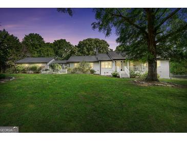 Charming white brick home with a lush green lawn and mature trees at dusk at 701 Mask Rd, Brooks, GA 30205