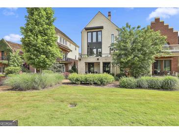 Landscaped backyard featuring manicured lawn, shrubs, trees and a modern home with a brick facade and black framed windows at 145 Kelmscott Ln, Fayetteville, GA 30214