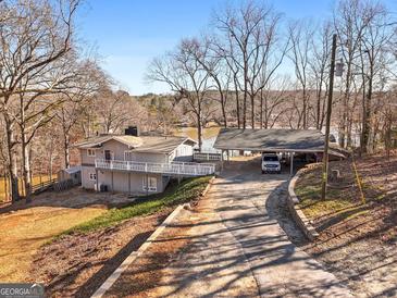 Waterfront home with carport, deck, and mature trees under a clear blue sky at 405 Miller Rd, Covington, GA 30014