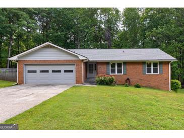 Charming brick home with a well-manicured lawn, attached garage, and lush green trees in the background at 295 Merrydale Dr, Fayetteville, GA 30215