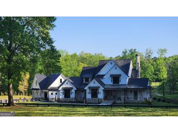 Stunning two-story modern farmhouse with a stone chimney, black metal roof and mature trees at 155 Green Meadow Ln, Fayetteville, GA 30215