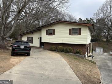 Split-level home with brick foundation, cream siding, brown trim, and a concrete driveway surrounded by trees at 2195 Wilson Nw Rd, Conyers, GA 30012
