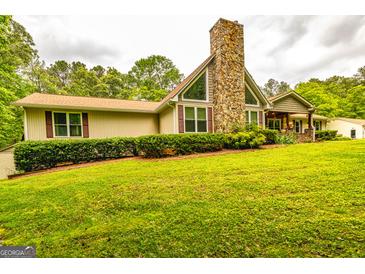 Charming home with a stone chimney, complemented by a lush green lawn and mature trees at 130 Brooklet Way, Brooks, GA 30205