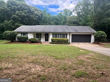 Charming single-story home featuring a dark roof, manicured shrubs, and an attached two-car garage at 120 Lazy Hollow Ln, Covington, GA 30016