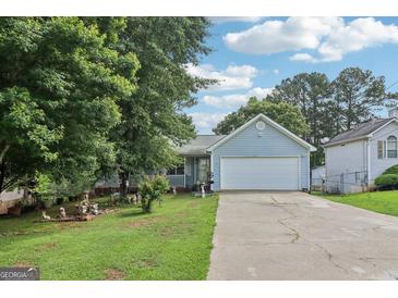 Charming, light blue single-story home featuring a two-car garage, manicured lawn and lush trees at 1152 Sunday Ln, Jonesboro, GA 30238