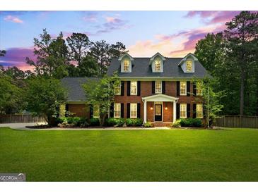 Elegant two-story brick home with a manicured lawn, black shutters, and dormer windows under a beautiful sunset sky at 171 Ponderosa Drive, Fayetteville, GA 30214