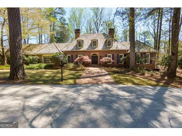 Charming brick home featuring a wood roof, dormer windows, mature trees, and a welcoming brick walkway at 9995 Huntcliff Trce, Atlanta, GA 30350