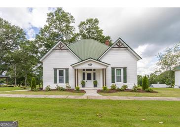 Charming white cottage with green metal roof, decorative shutters, and lush landscaped front yard at 111 S Old 27, Roopville, GA 30170