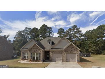 Charming brick home featuring an attached two-car garage, manicured lawn and a welcoming front entrance and stone patio at 1128 Carillon Se Dr, Conyers, GA 30013