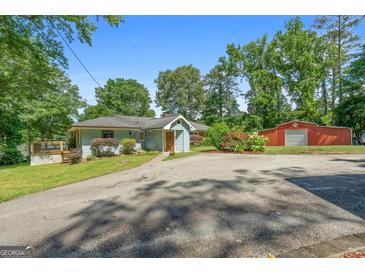 Charming single-story home with a well-manicured front yard, mature trees, and a red barn in the background at 312 Flat Shoals Church Rd, Stockbridge, GA 30281